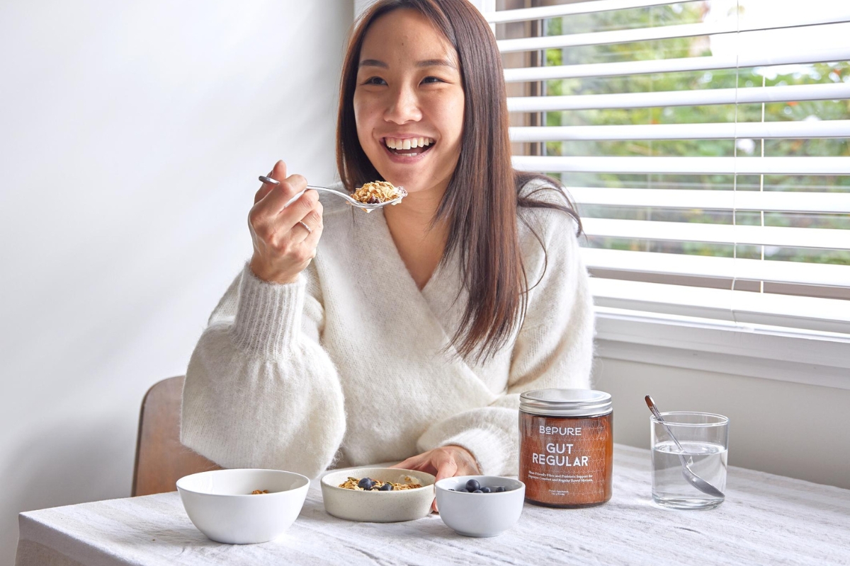 Woman at the breakfast table holding spoon with BePure Gut Regular on table