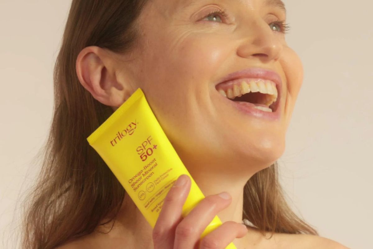 Smiling woman holding Trilogy SPF 50+ Omega-Boost Sunscreen