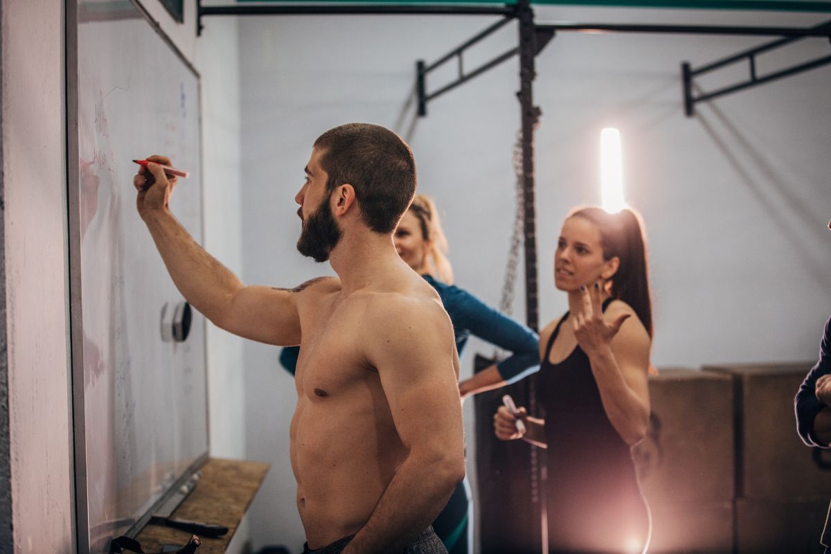 Group of people in a gym looking at a workout plan on the board