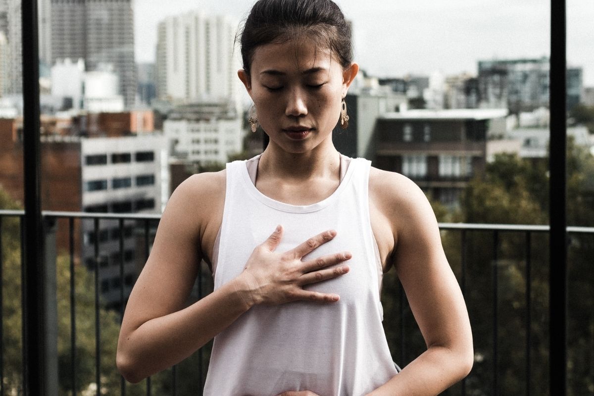 woman standing with eyes closed holding chest breathing